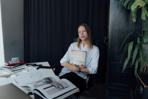 Mulher sentada em frente a uma mesa com livros olha para a câmera