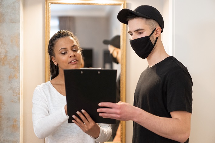 Relacionamento com o cliente Mulher negra de camisa branca e homem branco de camisa preta e máscara olham para prancheta