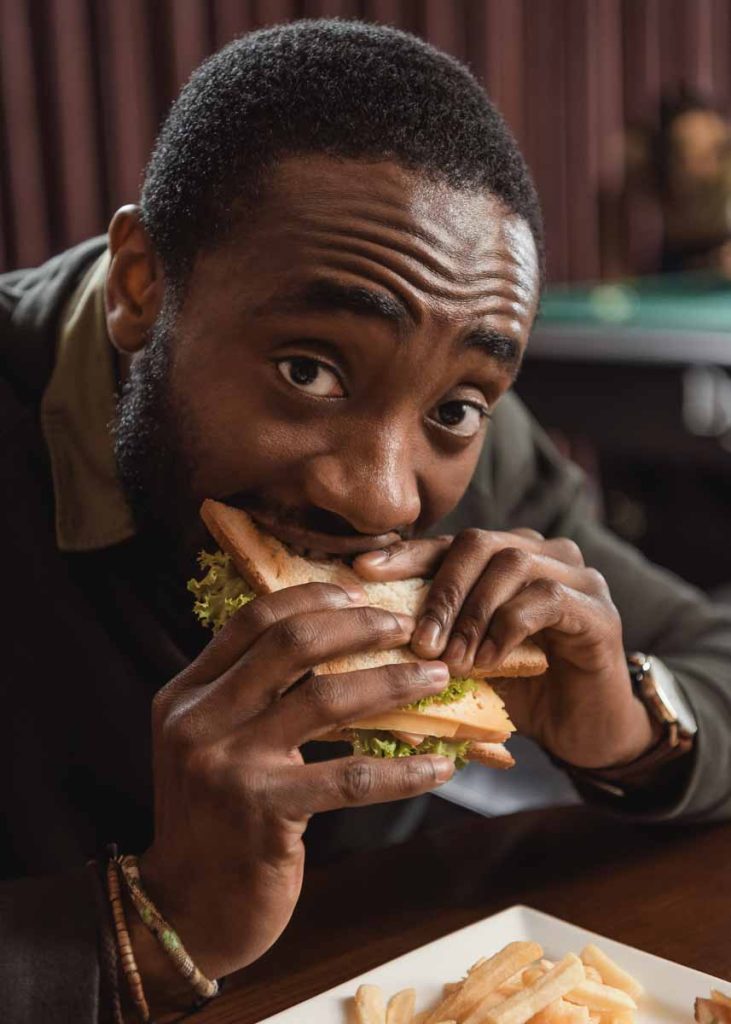 Homem negro comendo saunduíche no bar