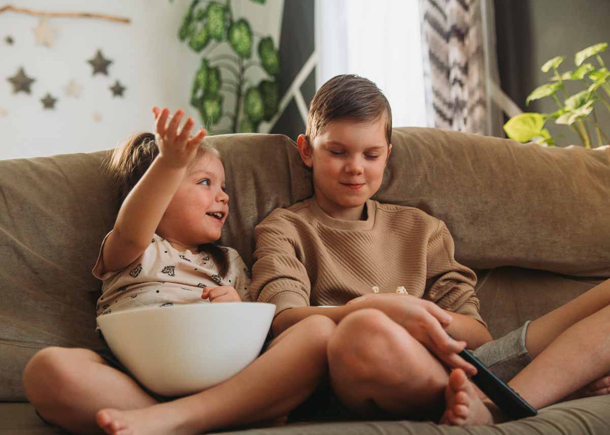 Menino e menina sentados no sofa com controle de televisão e bowl de pipoca