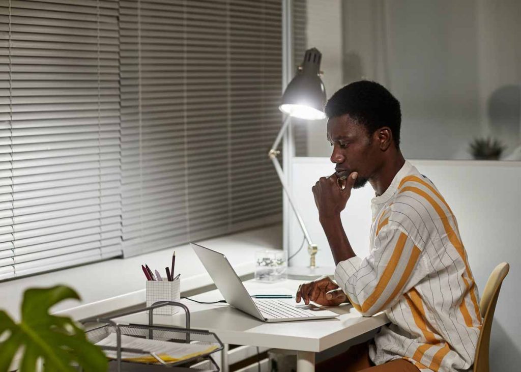 Retrato de homem negro com a mão no queixo estudando em um laptop