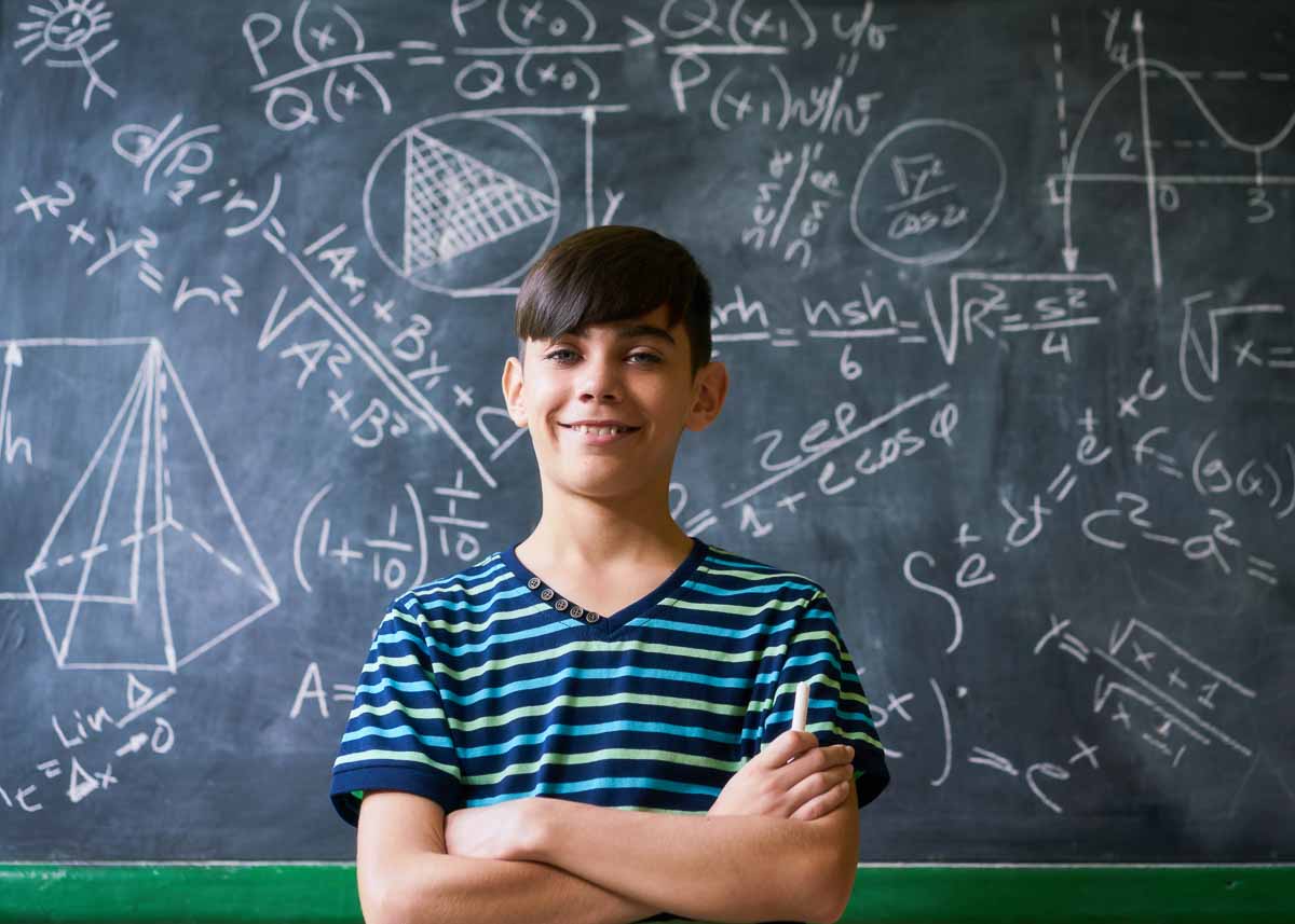 Conceito no quadro-negro na escola. Jovens, estudante e aluno em sala de aula. Garoto hispânico inteligente escrevendo fórmula matemática a bordo durante a aula. Retrato de criança do sexo masculino sorrindo, olhando para a câmera