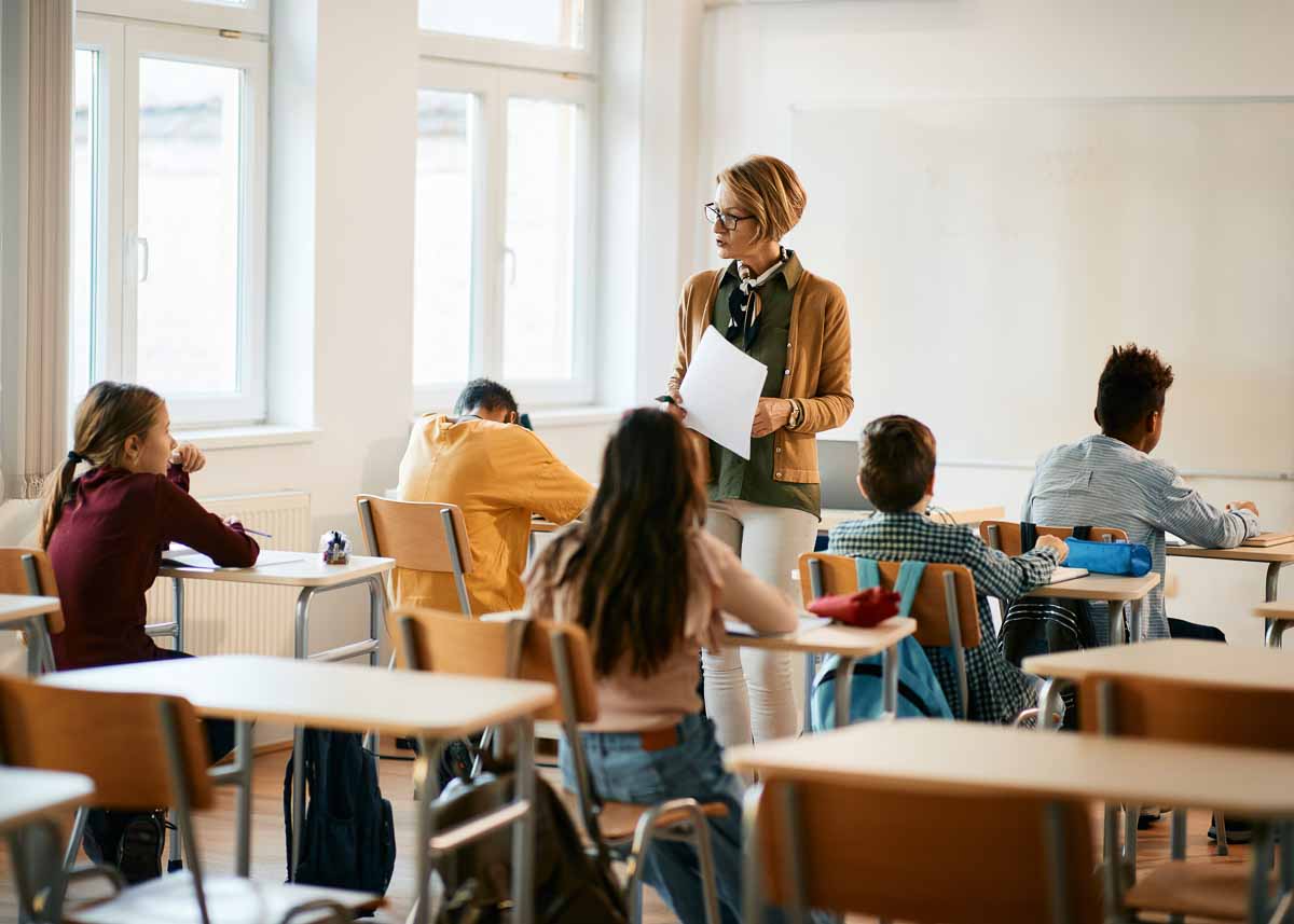 Professora sênior ensinando grupo de alunos do ensino fundamental em sala de aula. 